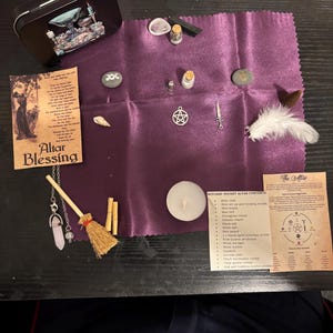 Pode incluir: Um kit de altar de bolso de bruxa com vários itens em um tecido roxo. Inclui uma lata de metal, cartões com texto, garrafas pequenas, cristais, um pingente de pentagrama, uma vassoura em miniatura, uma pena e uma vela de chá. O kit é projetado para práticas espirituais.