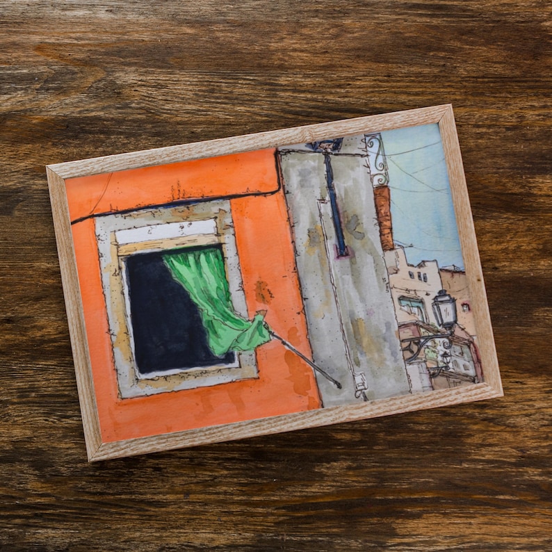 May include: A framed watercolor painting depicting an orange building facade with a dark window and a bright green curtain blowing in the breeze. The scene includes a gray wall section, a street lamp, and architectural details of nearby buildings.