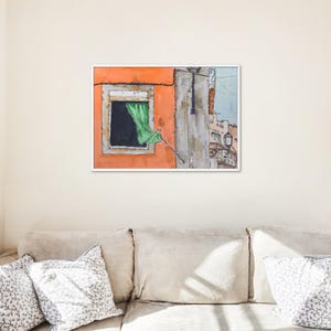 May include: A framed watercolor painting depicting an orange building facade with a single window. A green curtain hangs out of the window frame. The artwork includes architectural details of a street scene with a lantern and light blue sky.
