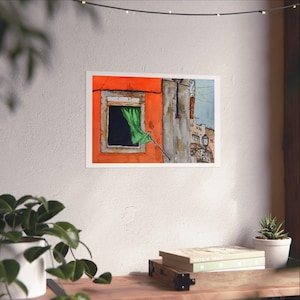 May include: A rectangular art print featuring a watercolor illustration of a bright orange building facade with a single window. A vibrant green curtain hangs from the window frame, and a glimpse of a neighboring stone structure is visible.