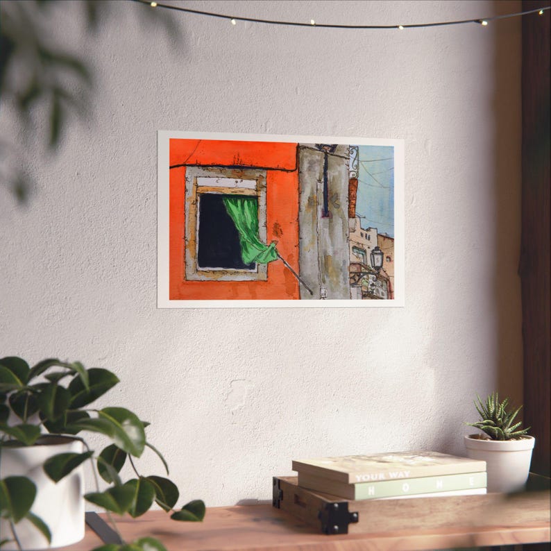May include: A rectangular art print featuring a watercolor illustration of a bright orange building facade with a single window. A vibrant green curtain hangs from the window frame, and a glimpse of a neighboring stone structure is visible.