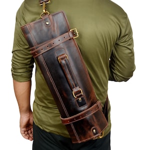 May include: A dark brown leather quiver with a shoulder strap and brass hardware. The quiver is cylindrical and features multiple leather straps with buckles. The leather has a distressed appearance.