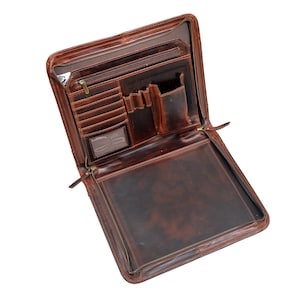May include: Open brown leather portfolio with multiple compartments, including card slots, pen holders, and a large interior pocket. The portfolio has a zip closure and a distressed finish, suggesting a vintage or rustic style.