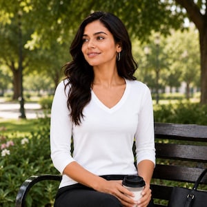 May include: A white long-sleeve shirt with a V-neckline paired with black trousers and a black tote bag. The shirt features three-quarter length sleeves and a fitted silhouette, providing a clean and simple look for various occasions.