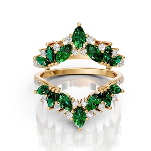 May include: Two gold rings with a leaf-like design. The rings feature marquise-cut emerald green gemstones and small white diamonds. The gemstones are set in a curved, v-shaped pattern.