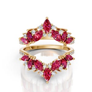 May include: Two gold rings with a V-shaped design. The rings are adorned with marquise-cut ruby gemstones and small round diamonds. The gemstones are a vibrant red color, and the diamonds sparkle against the gold.