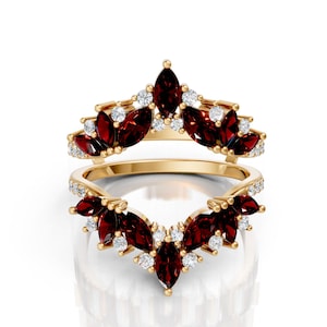 May include: Two-piece gold-toned ring set. The rings feature marquise-cut, deep red gemstones and small, round white gemstones. The gemstones are set in a floral or leaf-like pattern. The rings are displayed on a white background.