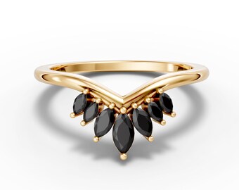 May include: A gold-colored ring with a V-shaped design. The ring features a series of black marquise-cut gemstones set along the V-shape. The ring is set against a white background.