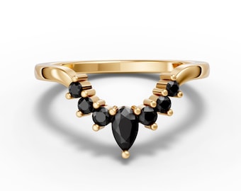 May include: A gold-colored ring with a curved design. The ring features a series of small, round black gemstones and a larger, teardrop-shaped black gemstone at the center. The ring is set against a white background.