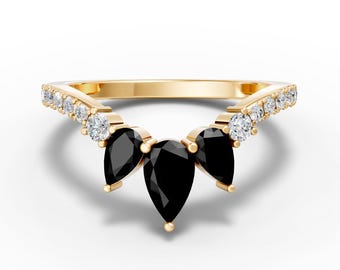 May include: A gold ring featuring three pear-shaped black gemstones in the center, flanked by smaller white gemstones. The ring has a delicate, curved design, with the gemstones set against a polished gold band.