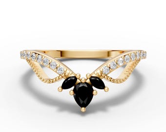 May include: A gold-colored ring with a unique design. The ring features a cluster of three black pear-shaped gemstones at the center, surrounded by smaller clear gemstones and a decorative band.
