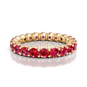 May include: A gold ring featuring a continuous row of vibrant red gemstones. The ring's band is a warm gold color, and the gemstones are evenly spaced, creating a circular pattern. The gemstones are a bright, saturated red.