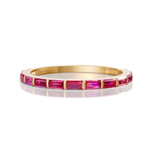 May include: A gold band ring featuring rectangular, vibrant pink gemstones. The gemstones are set closely together, creating a continuous line of color around the ring. The ring is displayed on a white background.