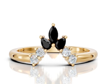 May include: A gold-colored ring featuring a crown design. The crown is adorned with three black marquise-cut stones and six smaller, round, clear stones. The ring has a smooth, polished band.