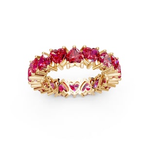 Könnte beinhalten: Ein goldfarbener Ring mit einem durchgehenden Band aus herzförmigen, leuchtend roten Edelsteinen. Das Design des Rings beinhaltet herzförmige Aussparungen entlang des Bandes, wodurch eine zarte und romantische Ästhetik entsteht. Die Edelsteine sind eng aneinander gesetzt und bilden einen vollen Kreis.