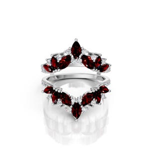 May include: Two silver rings with a floral design. Each ring features marquise-cut, deep red gemstones and small, round, clear gemstones. The rings are set against a white background.