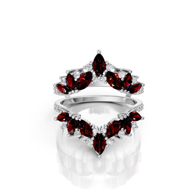 May include: Two silver rings with a floral design. Each ring features marquise-cut, deep red gemstones and small, round, clear gemstones. The rings are set against a white background.