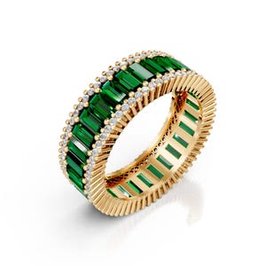May include: A gold ring featuring a band of emerald-cut green gemstones and small, round, clear gemstones. The ring has a textured gold band and is set against a white background.