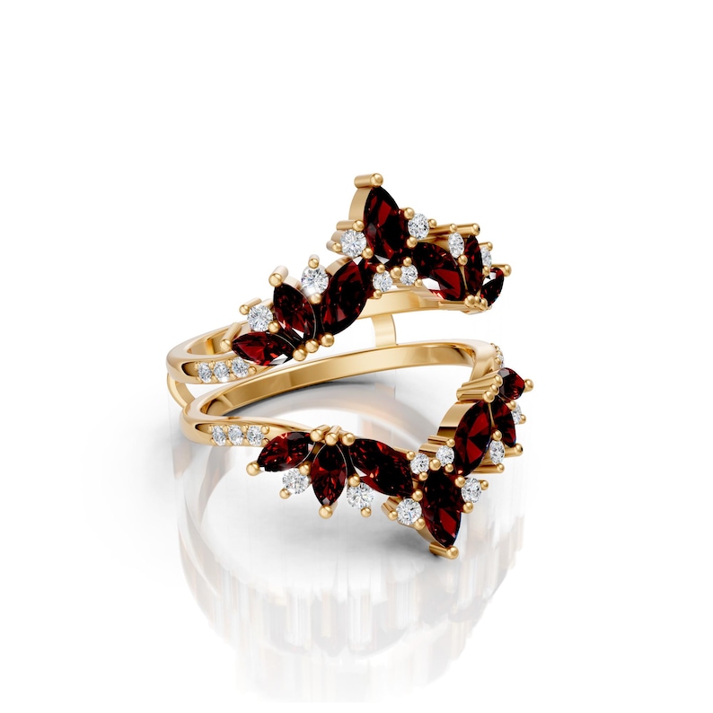 May include: A gold-colored ring with a unique design. The ring features marquise-cut, deep red gemstones and small, round, clear gemstones. The gemstones are arranged in a floral or leaf-like pattern. The ring has a split shank design.