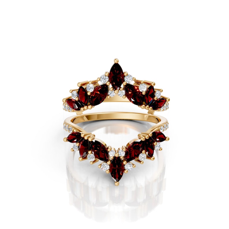 May include: Two-piece gold-toned ring set. The rings feature marquise-cut, deep red gemstones and small, round white gemstones. The gemstones are set in a floral or leaf-like pattern. The rings are displayed on a white background.