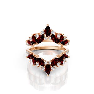 May include: Two-piece rose gold ring set. The rings feature marquise-cut, deep red gemstones and small, round white gemstones. The gemstones are set in a floral or leaf-like pattern. The rings are displayed on a white background.