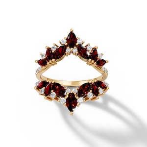 May include: A gold ring with a unique design. The ring features a series of marquise-cut, deep red gemstones and small, round, white gemstones. The gemstones are set in a floral or leaf-like pattern. The ring is set against a white background.