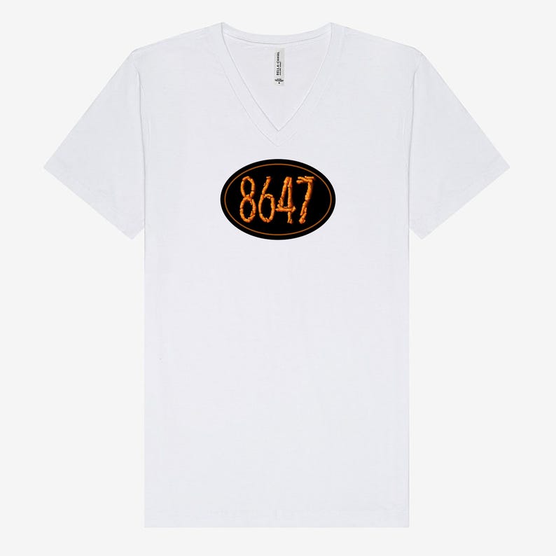 May include: White V-neck t-shirt with a black oval design in the center. The oval contains the number "8647" in a fiery orange font. The shirt has short sleeves and a relaxed fit.