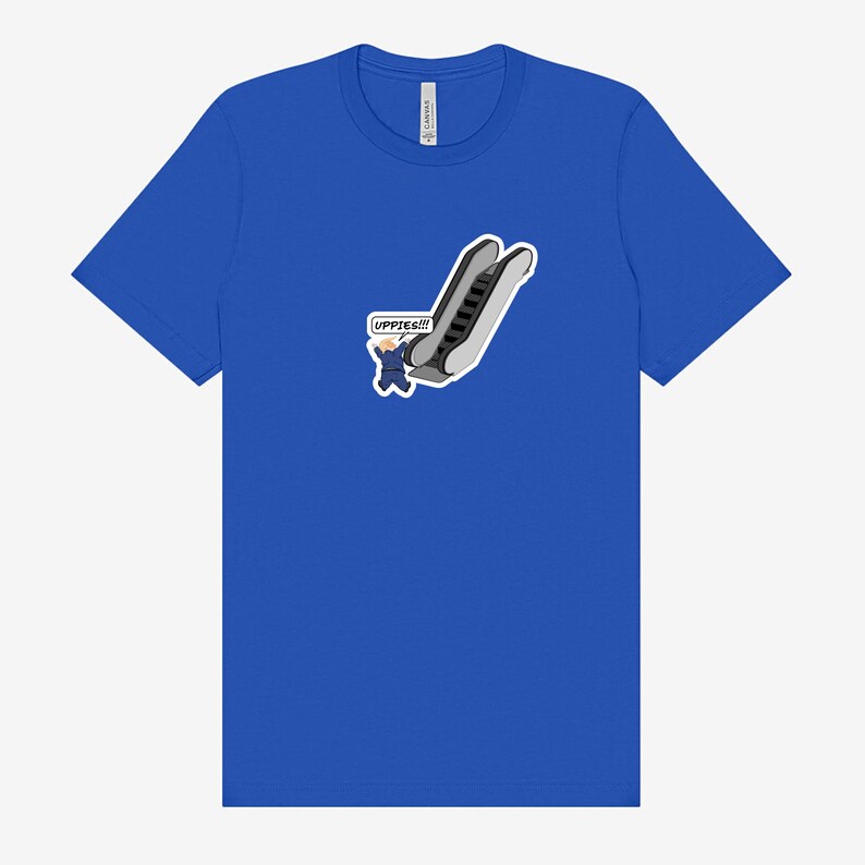 May include: Royal blue t-shirt featuring a cartoon graphic of an escalator with a person waving and the word "UPPIES!!!" in a speech bubble. The graphic is in shades of gray, black, and blue.