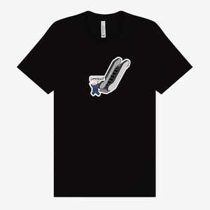 May include: Black t-shirt featuring a cartoon graphic of an escalator with a person in a blue suit and the text "UPPIES!!!" in a speech bubble. The graphic is in shades of gray, white, and blue.