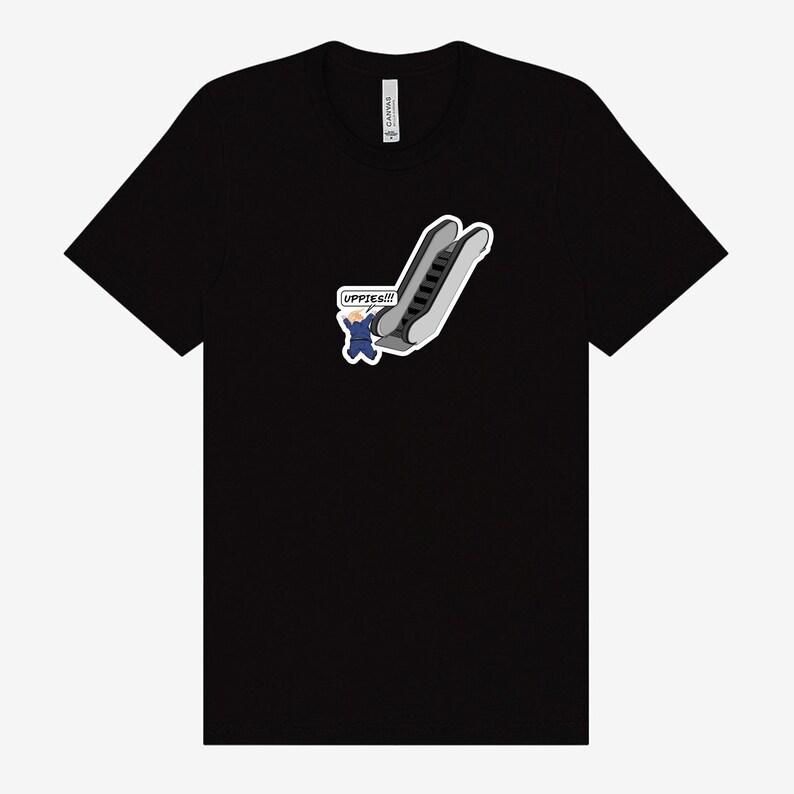 May include: Black t-shirt featuring a cartoon graphic of an escalator with a person in a blue suit and the text "UPPIES!!!" in a speech bubble. The graphic is in shades of gray, white, and blue.
