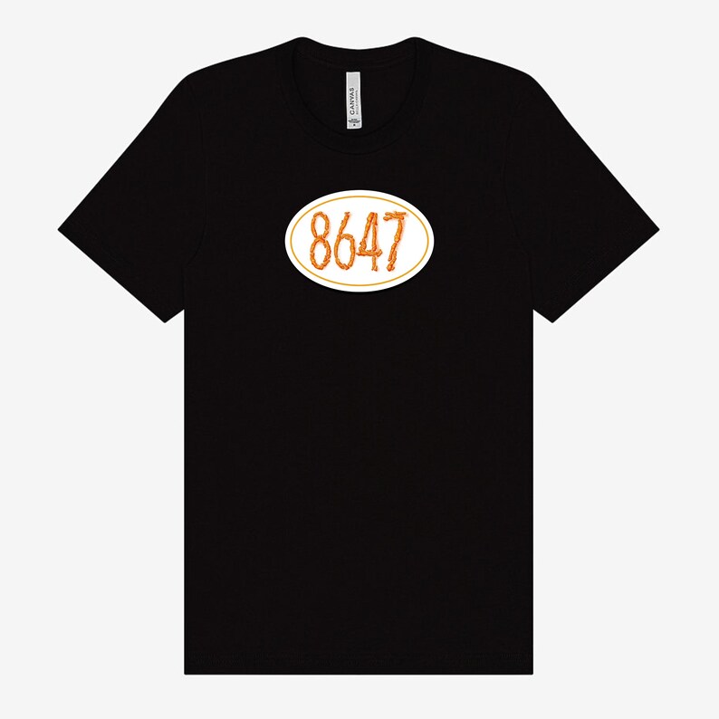 May include: Black t-shirt featuring an oval design with the number "8647" in a textured orange font, outlined in white. The shirt is made of a soft material and has a crew neck.
