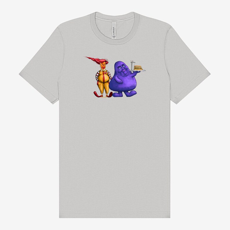 May include: Light gray t-shirt featuring a cartoon illustration of two characters. One character is purple and holding a tray with a burger. The other character is yellow and red. The shirt is made of a soft material.