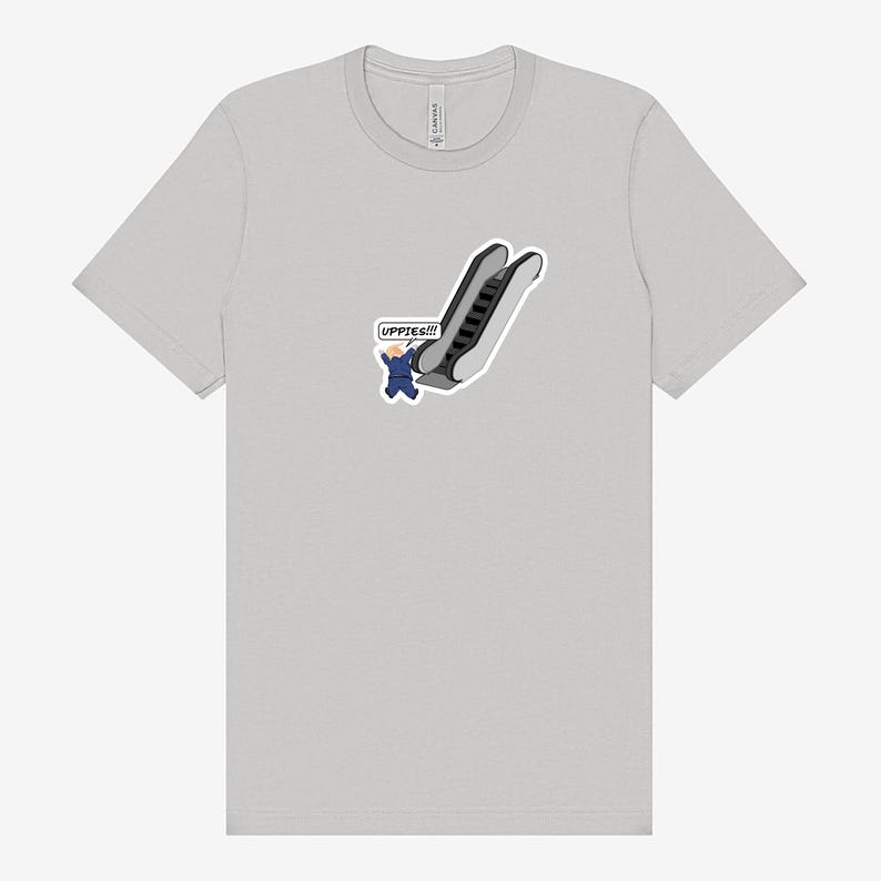 May include: A light gray t-shirt featuring a cartoon of a person in a blue suit falling down an escalator. The text "UPPIES!!!" is in a speech bubble. The shirt is a basic crew neck.