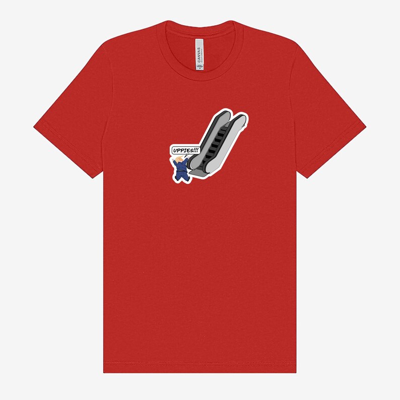 May include: Red t-shirt featuring a cartoon graphic of a person in a blue suit falling down an escalator. The text "UPPIES!!!" is in a speech bubble. The shirt is made of a soft material.
