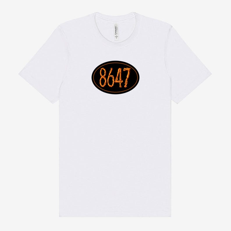 May include: White t-shirt with a black oval design in the center. The oval contains the number "8647" in a stylized orange font. The shirt has a crew neck and short sleeves.