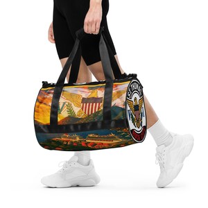 May include: A cylindrical duffel bag featuring a vibrant sunset scene with a shield and eagle emblem. The bag has black handles and a patch that reads "ST. THOMAS ROCK CITY".