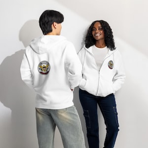 May include: White zip-up hoodies with a circular emblem featuring an eagle, shield, and text. The hoodies are worn by two people, one in light-wash jeans and the other in dark blue cargo pants.