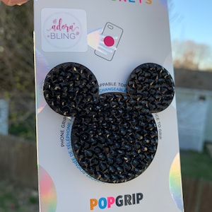 May include: Black rhinestone Mickey Mouse PopSocket phone grip with the words "PopSockets", "adora BLING", "APPABLE TOP CHANGEABLE", "PHONE GRIP", "ICE TO GRIP", and "POPGRIP" printed on the packaging.