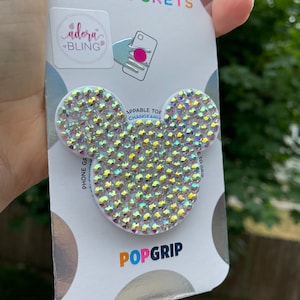 May include: A white PopSockets PopGrip with a clear, iridescent, crystal-covered Mickey Mouse head design. The packaging features the words "PopSockets", "PopGrip", and "Apppable Top Change-a-Grip".