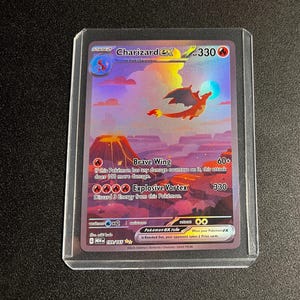 May include: A Charizard EX Pokémon trading card, stage 2, featuring a flying orange dragon over a landscape with a volcano. The card has text including "Brave Wing" and "Explosive Vortex". The card is in a protective sleeve.