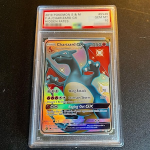 May include: A graded Charizard GX Pokémon card from the Hidden Fates set. The card features a blue and orange Charizard illustration with the text "Wing Attack" and "Crimson Storm". The card is encased in a clear protective holder with a red label.