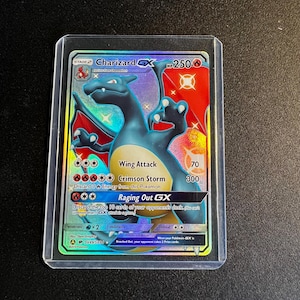 May include: A Charizard GX Pokémon trading card, featuring a blue and orange dragon with the text "Wing Attack" and "Crimson Storm." The card is encased in a protective sleeve. The card has a HP of 250.