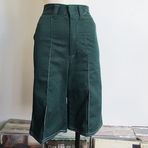 May include: Dark green culottes with white stitching details. The high-waisted shorts have a button and zipper closure and are displayed on a mannequin. The culottes have a wide leg design.