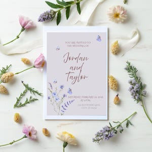Può includere: Un invito di nozze con i nomi "Jordan e Taylor" in una scrittura elegante. L'invito è adornato da elementi floreali, tra cui fiori rosa e gialli, rametti e un nastro bianco. Il testo recita "Siete invitati al matrimonio di" e la data.
