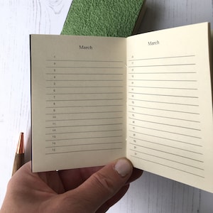 May include: A small, cream-coloured notebook with a black cover and the word "March" printed on the front. The notebook is open to the month of March, with numbered days and lines for writing.