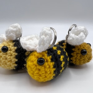 May include: Three crocheted bee keychains with black and yellow striped bodies, white wings, and black button eyes.