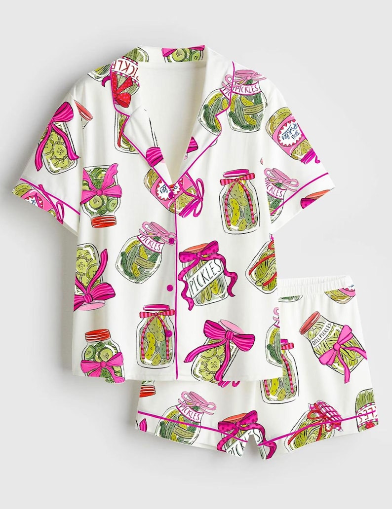 Puede incluir: Conjunto de pijama blanco con un estampado de tarros de pepinillos. La camiseta de manga corta y los pantalones cortos presentan un dise&ntilde;o repetido de tarros de pepinillos con lazos rosas y la palabra "Pickles". El ribete es rosa.