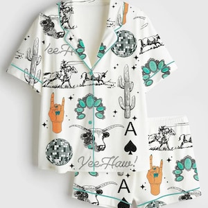 May include: White pajama set with a short-sleeved button-up shirt and shorts. The set features a turquoise trim and a repeating pattern of cacti, disco balls, longhorn skulls, and the text "Yee Haw!" and "A".