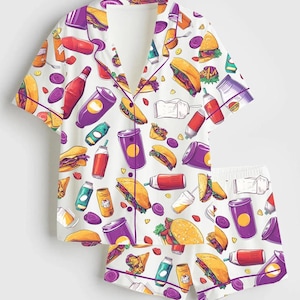 May include: White pajama set with a colorful fast food print. The short-sleeved top and shorts feature illustrations of burgers, tacos, soda cans, and other food items. The set has purple trim.