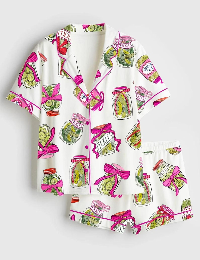 Puede incluir: Conjunto de pijama blanco con un estampado de tarros de pepinillos. La camiseta de manga corta y los pantalones cortos presentan un dise&ntilde;o repetido de tarros de pepinillos con lazos rosas y la palabra "Pickles". El conjunto tiene ribetes rosas.